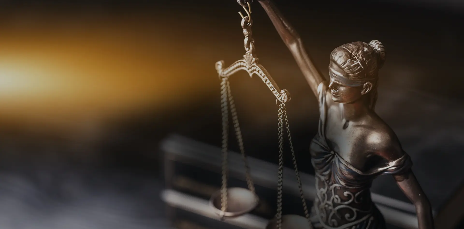 Bronzene Justitia‑Statue mit Waage vor warmem Licht – Symbol für Recht und Fairness, ohne eingeblendeten Text.